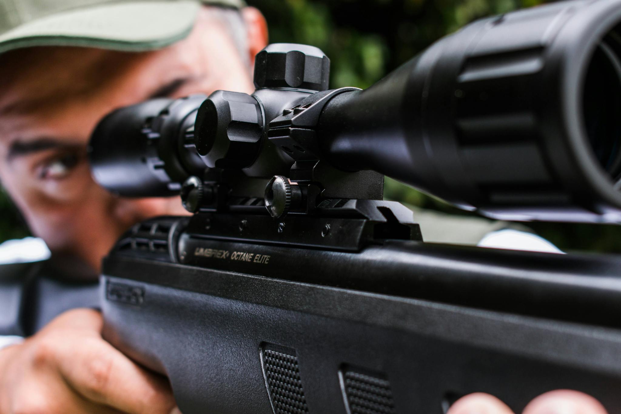 Focused man aiming through a sniper rifle scope outdoors, showcasing precision.